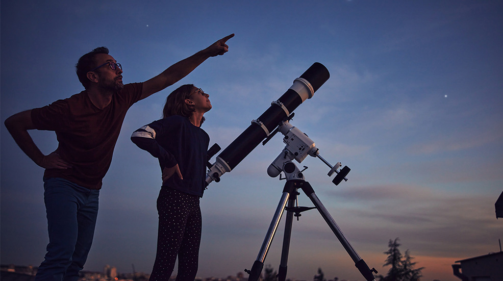A father and daughter using an astronomical telescope to look up at the stars